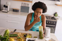 Mid Adult African American Woman Licking Finger While Drinking Healthy Juice In Kitchen At Home