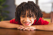 © Wavebreak Media - Portrait of happy hispanic boy with curly black hair leaning on table at home