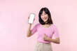 © Jirawatfoto - Portrait beautiful young asian woman happy smile showing smartphone screen with pointing finger hand gesture to mobile phone isolated on pink pastel studio background. Blank screen smartphone concept