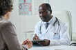 © pressmaster - Mature African American clinician with medical document listening to female patient describing her symptoms during consultation