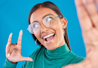 Wall Mural - Woman, face and fashion selfie with rock on hand for gen z attitude on a blue background with glasses. Happy model person in studio with excited and cool hand sign or emoji with beauty and motivation