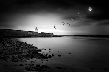 Georgian Lighthouse at Burry Port Carmarthenshire South Wales near the Gower Peninsula at night with a moon and ducks in flight, stock photo black and white monochrome image