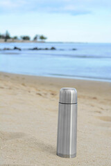 Canvas Print - Metallic thermos with hot drink on sandy beach near sea, space for text