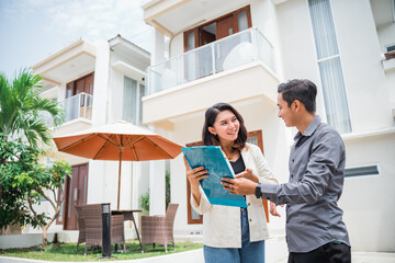 female employee of an estate agent showing clipboard chatting with man in residential background