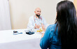 © IHERPHOTO - Back view of a female patient talking to the nutritionist. Smiling nutritionist explaining to a female patient, Nutritionist man talking to woman patient in office