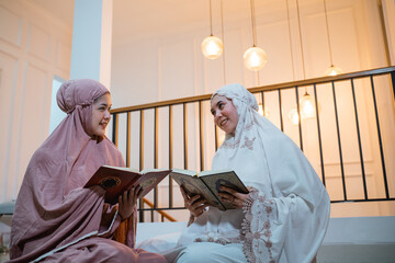 two Asian girls in hijab chat while reciting Quran in prayer room at home