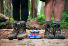 Expecting Parents Use A Pair Of Small Hiking Boots In Line With Their Own To Announce The Arrival Of Their New Baby.