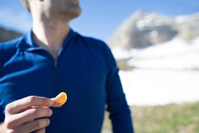 A Man Holds A Dried Mandarin Orange As Trail Food On A Bright Day.