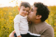 © Cavan Images - Toddler son smiles while Latino Dad kisses cheek outside in field