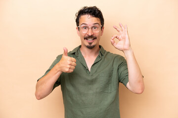 Wall Mural - Young caucasian man isolated on beige background showing ok sign and thumb up gesture