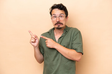 Wall Mural - Young caucasian man isolated on beige background frightened and pointing to the side