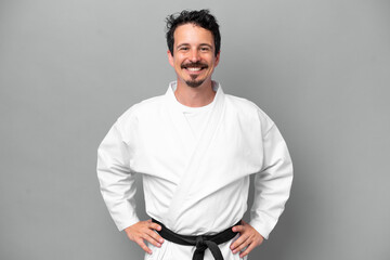 Wall Mural - Young caucasian man isolated on grey background doing karate posing with arms at hip and smiling