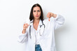 © luismolinero - Young caucasian woman isolated on white background wearing a doctor gown and holding pills while doing bad signal