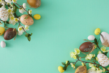 Wall Mural - Easter decoration concept. Flat lay photo of colorful easter eggs and cherry blossom branches on teal background with empty space in the middle