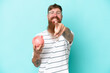 Redhead man with long beard holding a piggybank isolated on blue background points finger at you with a confident expression