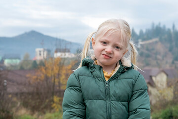 Portrait of pensive blonde girl with two tails standing in fresh air of countryside. Vacation with children in autumn