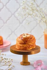 Wall Mural - Yeast dough cruffin with salted caramel and hazelnuts on a wooden stand on a light wooden background.