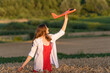 © somemeans - Happy young woman with toy airplane in hands in middle of wheat field, in red dress and white shirt Concept of cheap air travel