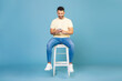 © Home-stock - Young man using smartphone, chatting online, browsing social media, sitting on chair on blue background, full length