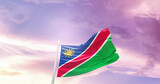 Fototapeta  - Waving Flag of Namibia in Blue Sky. The symbol of the state on wavy cotton fabric.