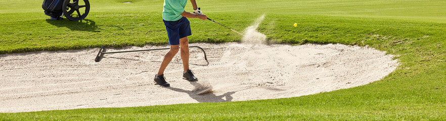 The golf player hits the ball from the bunker with a golf club, on a sunny day in summer.