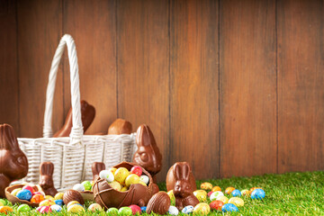 Wall Mural - Easter egg hunting background. Various candy and chocolate Easter eggs, bunny and rabbits with basket for eggs on green grass park or garden background