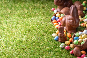 Wall Mural - Easter egg hunting background. Various candy and chocolate Easter eggs, bunny and rabbits with basket for eggs on green grass park or garden background