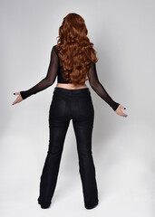 Canvas Print - Full length portrait of beautiful woman with long red hair wearing black corset top and leather pants. Standing pose, facing backwards walking away from camera. Isolated on white studio background.