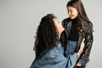 Smiling tattooed mother hugging daughter isolated on grey.