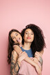 Smiling girl sticking out tongue while hugging curly mother on pink background.