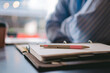 © juanpablo - Close-up of a pen on top of an agenda with a man's crossed arms blurred in the background.
