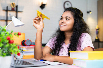 girl holding paper plane dreaming about foreign or abroad study while reading or preparing for examination - concept of future career, imagination and education