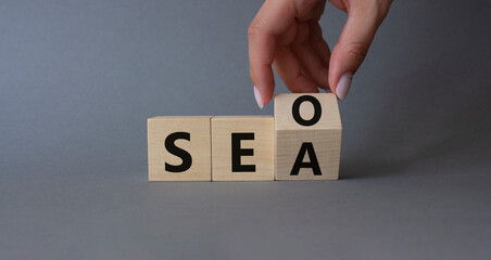 SEO vs SEA symbol. Businessman hand Turnes cube and changes word SEA to SEO. Beautiful grey background. Business and SEO vs SEA concept. Copy space