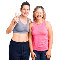 Couple of women wearing sportswear showing and pointing up with fingers number two while smiling confident and happy.