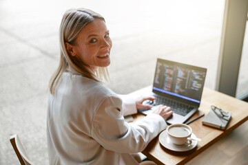 Wall Mural - Business lady working on laptop and drinking coffee while sitting in cafe near window. Distance work