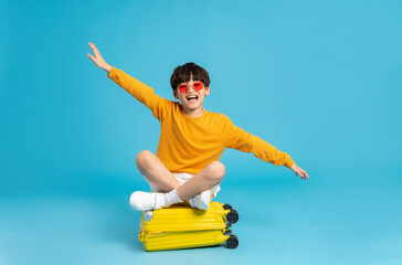 Wall Mural - Asian boy pulling suitcase on blue background