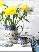 A Ceramic Mug With Tea And A Jug With Astromelia Flowers And Daffodils On A White Bedside Table Near The Bed. Selective Focus On The Mug.