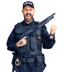 Poster - Young handsome man wearing police uniform holding shotgun screaming proud, celebrating victory and success very excited with raised arms