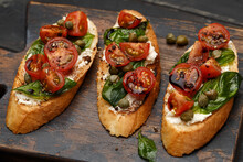 Traditional Italian Bruschetta With Cherry Tomatoes, Cream Cheese, Basil Leaves, Capers And Balsamic Vinegar On Wooden Cutting Board. Close Up View