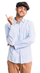 Sticker - Young hispanic man wearing casual shirt with a big smile on face, pointing with hand and finger to the side looking at the camera.