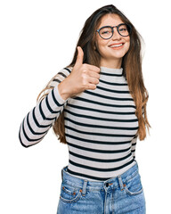 Canvas Print - Young beautiful teen girl wearing casual clothes and glasses doing happy thumbs up gesture with hand. approving expression looking at the camera showing success.