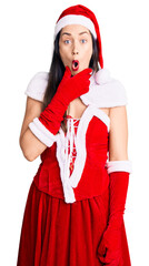 Wall Mural - Young beautiful caucasian woman wearing santa claus costume looking fascinated with disbelief, surprise and amazed expression with hands on chin