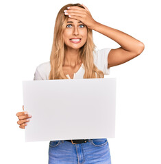 Sticker - Beautiful blonde young woman holding blank empty banner stressed and frustrated with hand on head, surprised and angry face