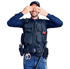 Canvas Print - Young handsome man wearing police uniform covering eyes with hands smiling cheerful and funny. blind concept.