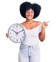 Sticker - Young african american girl holding big clock smiling happy pointing with hand and finger to the side