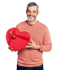 Poster - Middle age hispanic with grey hair holding valentine gift looking positive and happy standing and smiling with a confident smile showing teeth