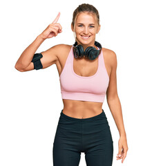 Wall Mural - Young blonde woman wearing gym clothes and using headphones pointing finger up with successful idea. exited and happy. number one.