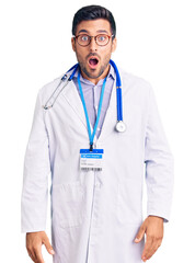 Wall Mural - Young hispanic man wearing doctor uniform and stethoscope afraid and shocked with surprise and amazed expression, fear and excited face.