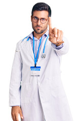 Wall Mural - Young hispanic man wearing doctor uniform and stethoscope pointing with finger up and angry expression, showing no gesture