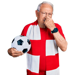 Canvas Print - Senior man with grey hair football hooligan holding ball smelling something stinky and disgusting, intolerable smell, holding breath with fingers on nose. bad smell